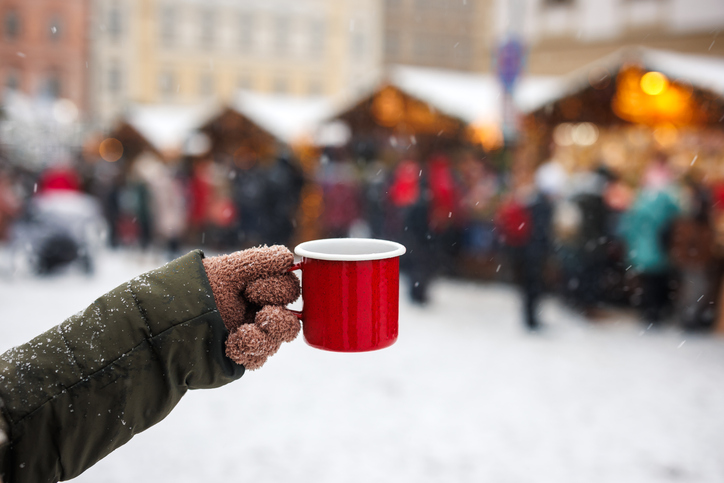 Die 5 schönsten Weihnachtsmärkte in der Eifel. Frau genießt Glühwein oder Punsch in einem roten Becher auf einem traditionellen Weihnachtsmarkt