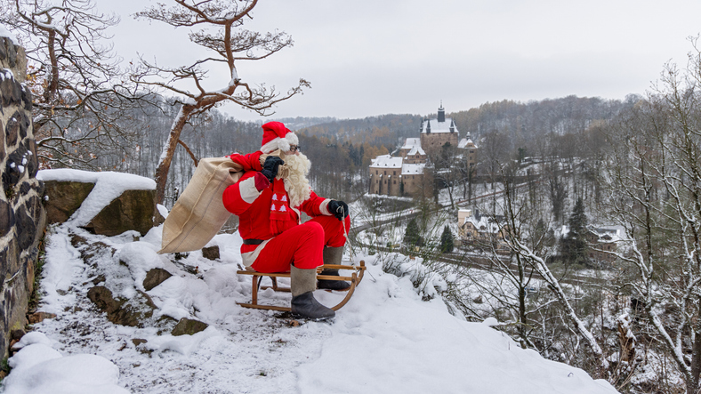 Die 5 schönsten Weihnachtsmärkte in der Eifel. Ein Weihnachtsmann sitzt mit einem Sack voller Geschenke auf einem Schlitten in einer winterlichen Landschaft
